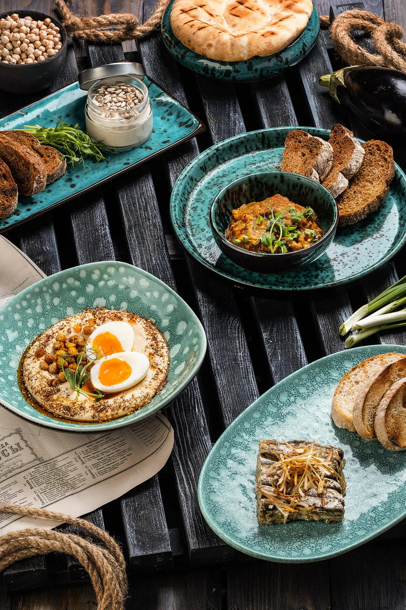 Hummus with eggs, eggplant dip, pita and bread on teal plates, photo by Alex Slyadnev