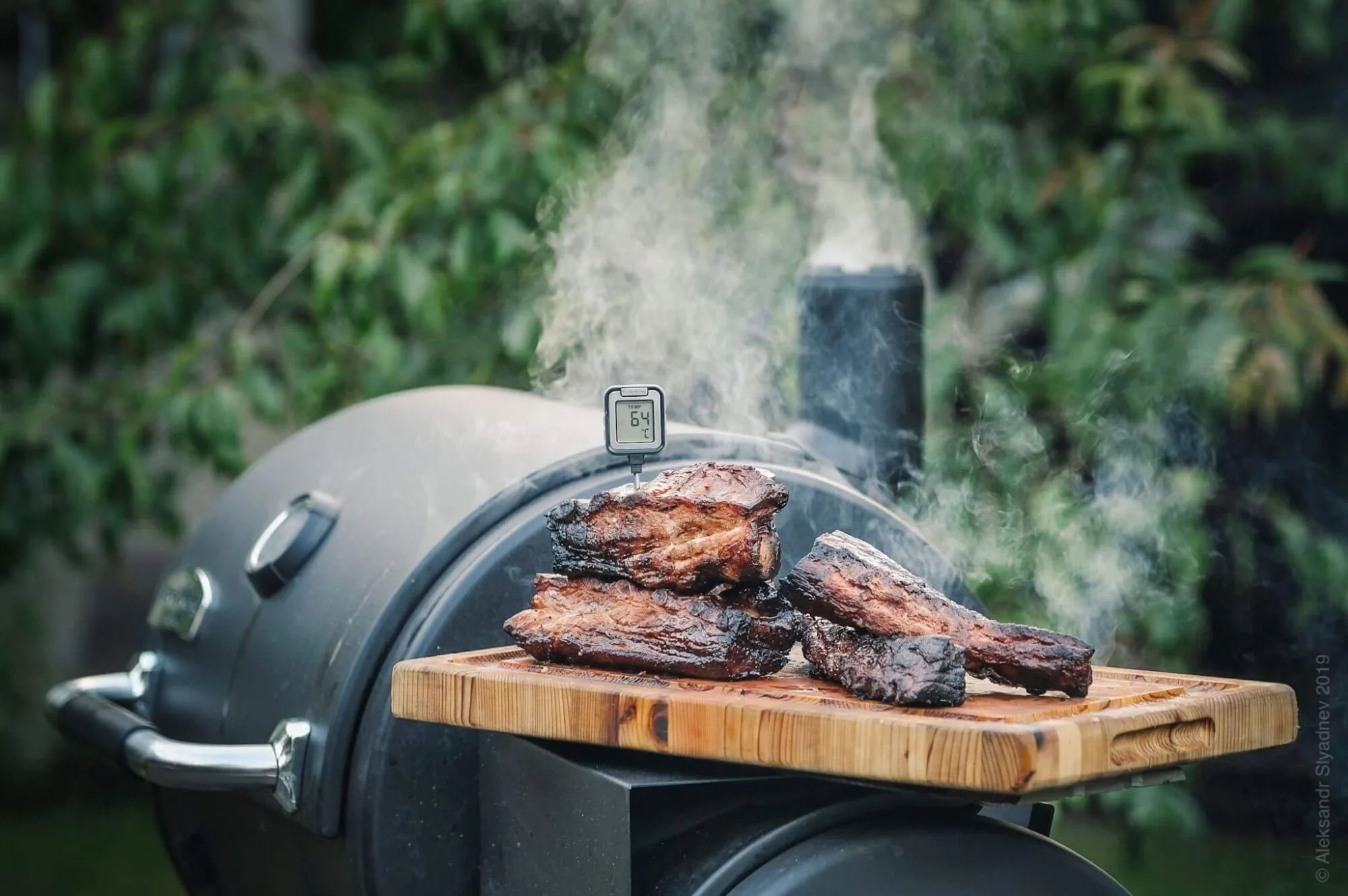 Smoked barbecue ribs on a cutting board over a smoker, by Alex Slyadnev