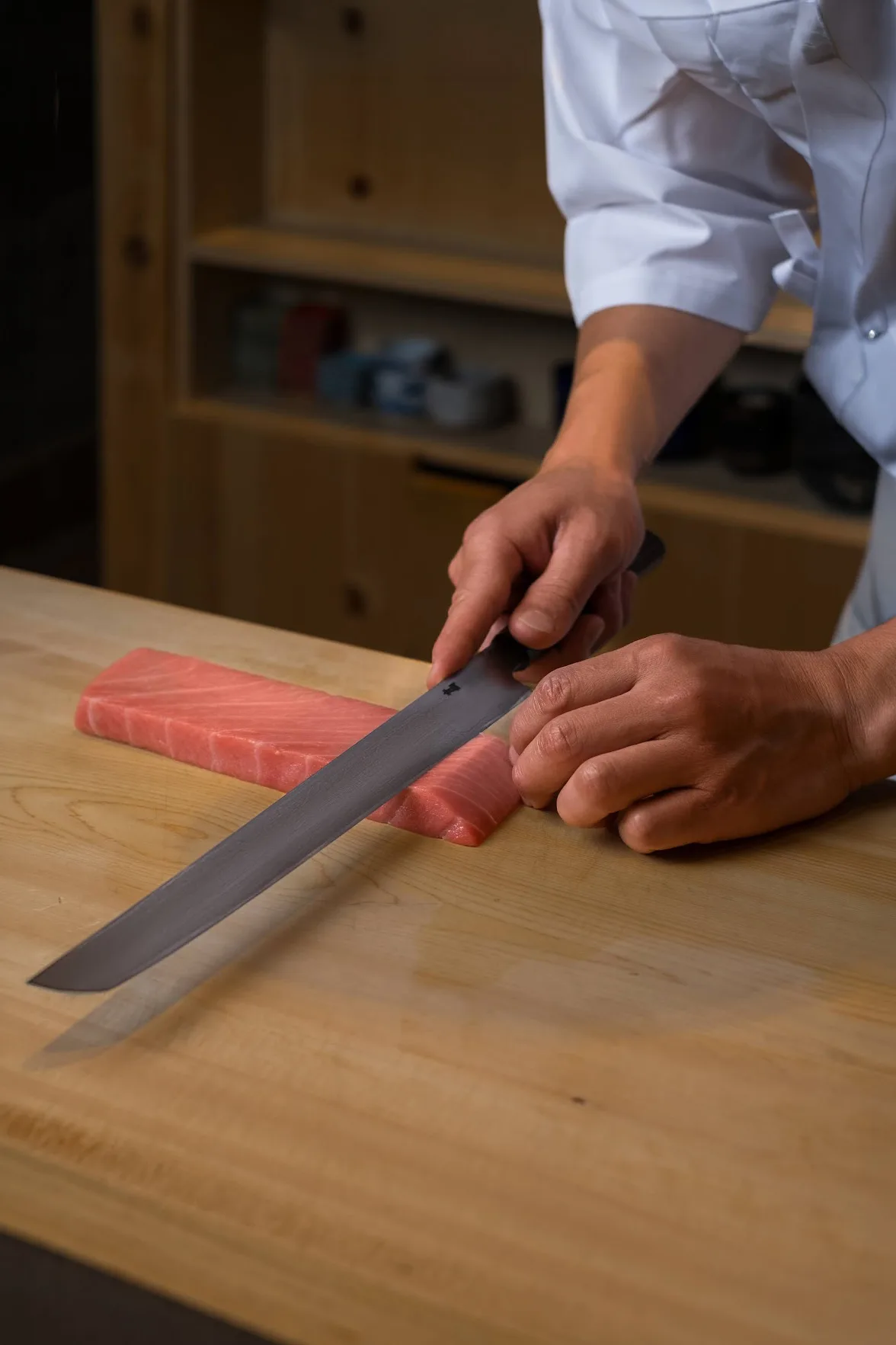 Sushi chef slicing a block of fresh tuna with a Japanese knife, photo by Alex Slyadnev