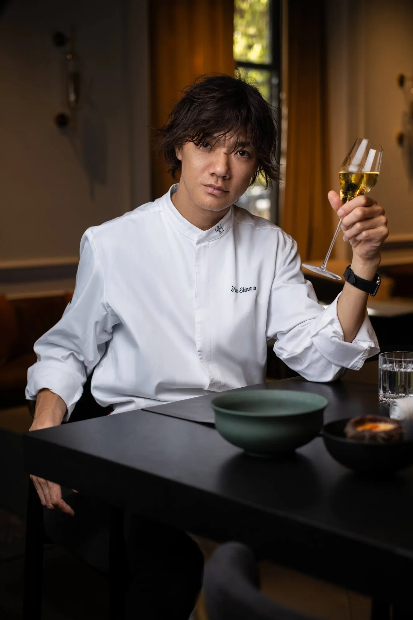 Chef in white jacket holding a glass of champagne, restaurant portrait, photo by Alex Slyadnev