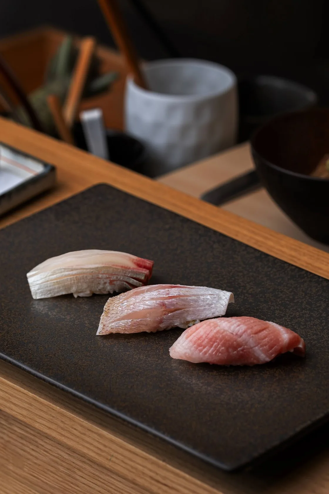 Three pieces of nigiri sushi on a dark stone plate, photo by Alex Slyadnev