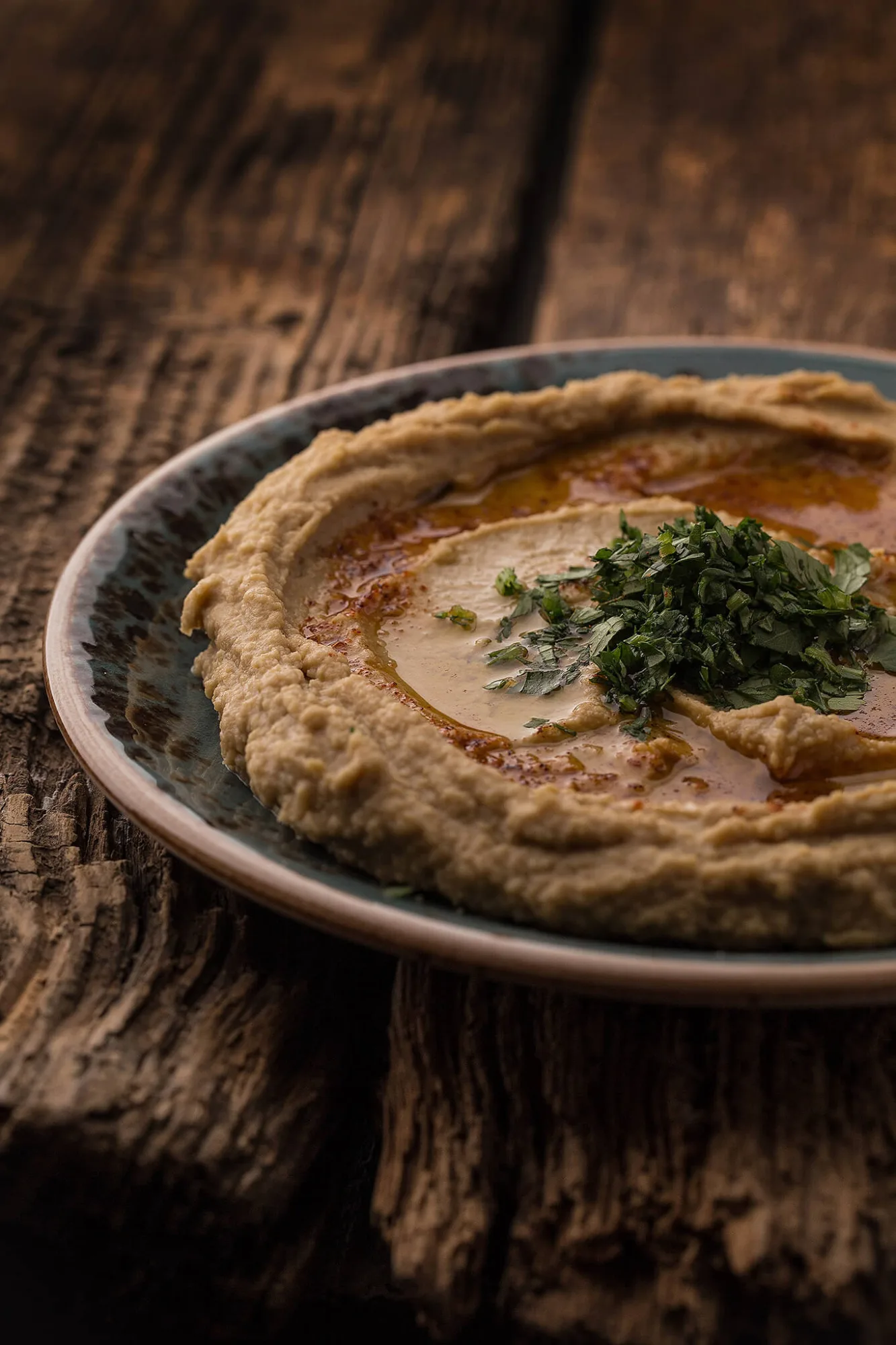Hummus with olive oil and parsley on rustic wood, by Alex Slyadnev