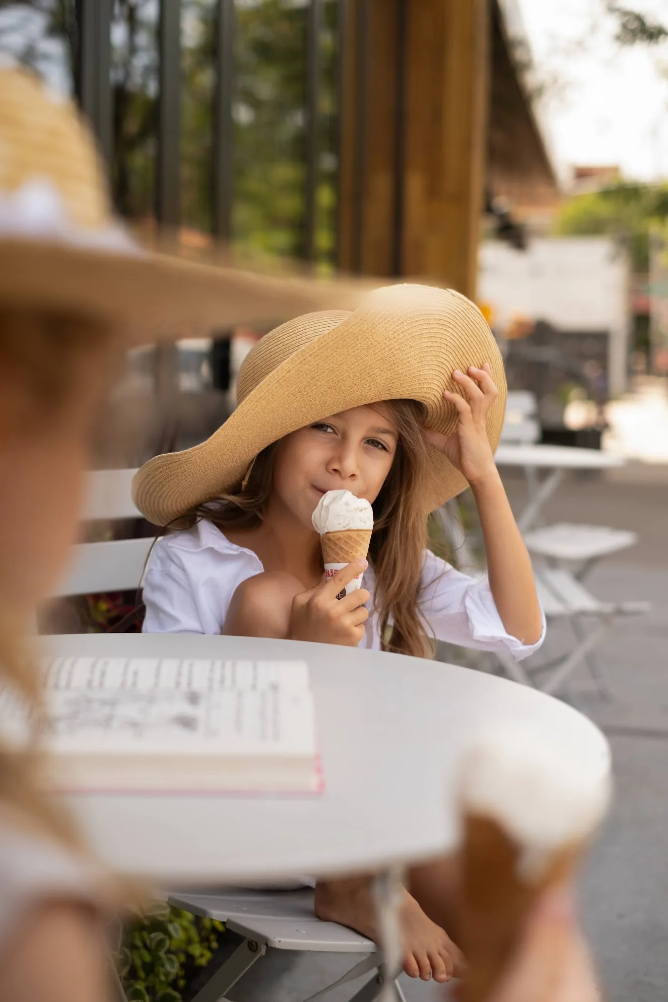 Girl in a straw hat eating an ice cream cone at a cafe table, photo by Alex Slyadnev