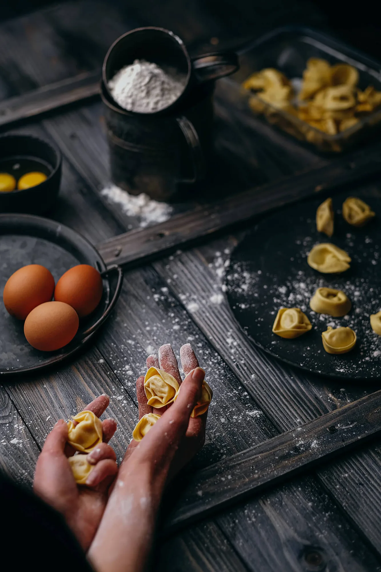 Hands holding homemade tortellini with flour and eggs on wooden table, photo by Alex Slyadnev